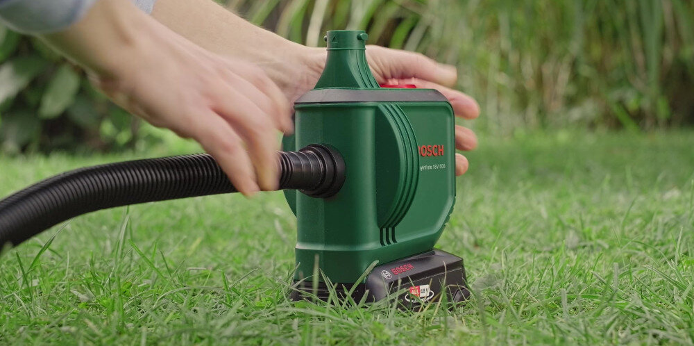 Osoba używa zielonej pompki akumulatorowej BOSCH na trawie. Na urządzeniu widoczne jest logo BOSCH oraz napis \'EasyInflate 18V-500\'.