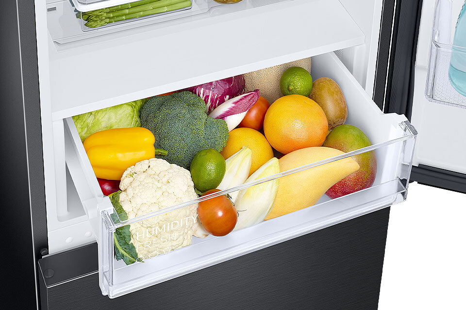 Kalafior, papryka i mango przechowywane w szufladzie dedykowanej owocom i warzywom Wnętrze lodówki z otwartą szufladą wypełnioną różnorodnymi warzywami i owocami, takimi jak brokuł, kalafior, papryka, pomidor, cytrusy i mango. Na szufladzie widoczny jest napis \'HUMIDITY FRESH\'.