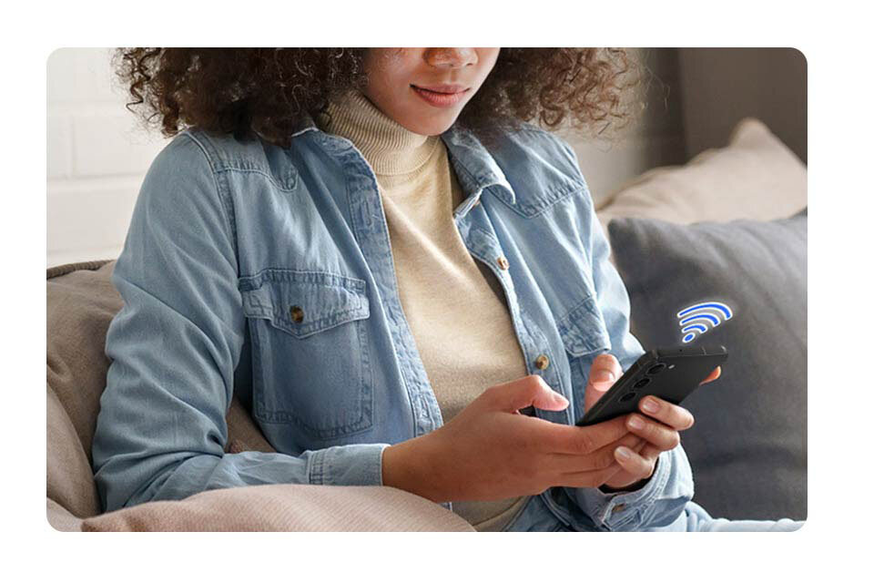 połączenie z aplikacją Osoba siedzi na kanapie, trzymając w rękach smartfon z ikoną sygnału Wi-Fi nad nim. Ubrana jest w jasnoniebieską koszulę i beżowy golf.