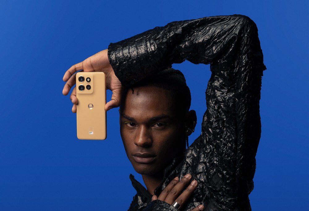 Osoba trzymająca smartfon w kolorze złotym z czterema aparatami na niebieskim tle. Na telefonie widoczne jest logo producenta.