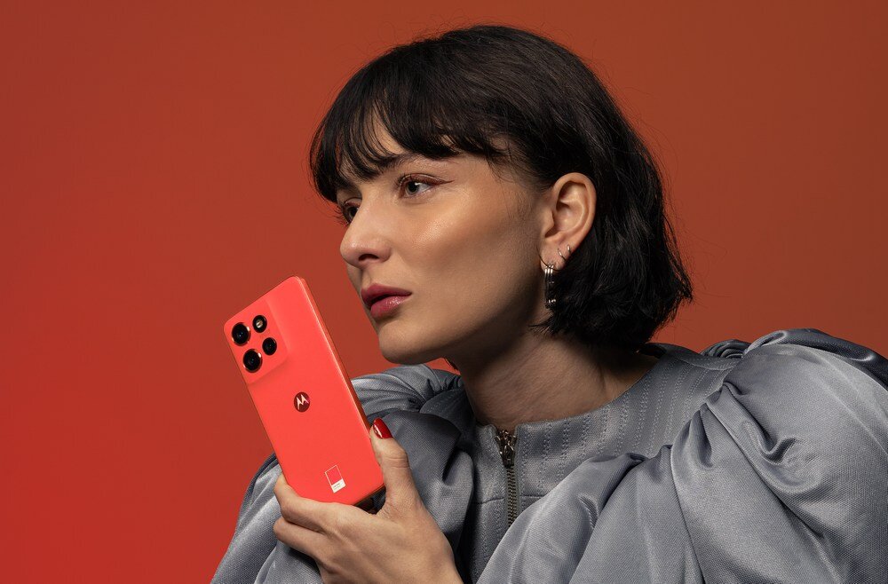 Osoba trzyma czerwony smartfon z logo Motorola na pomarańczowym tle. Telefon ma cztery kamery z tyłu.