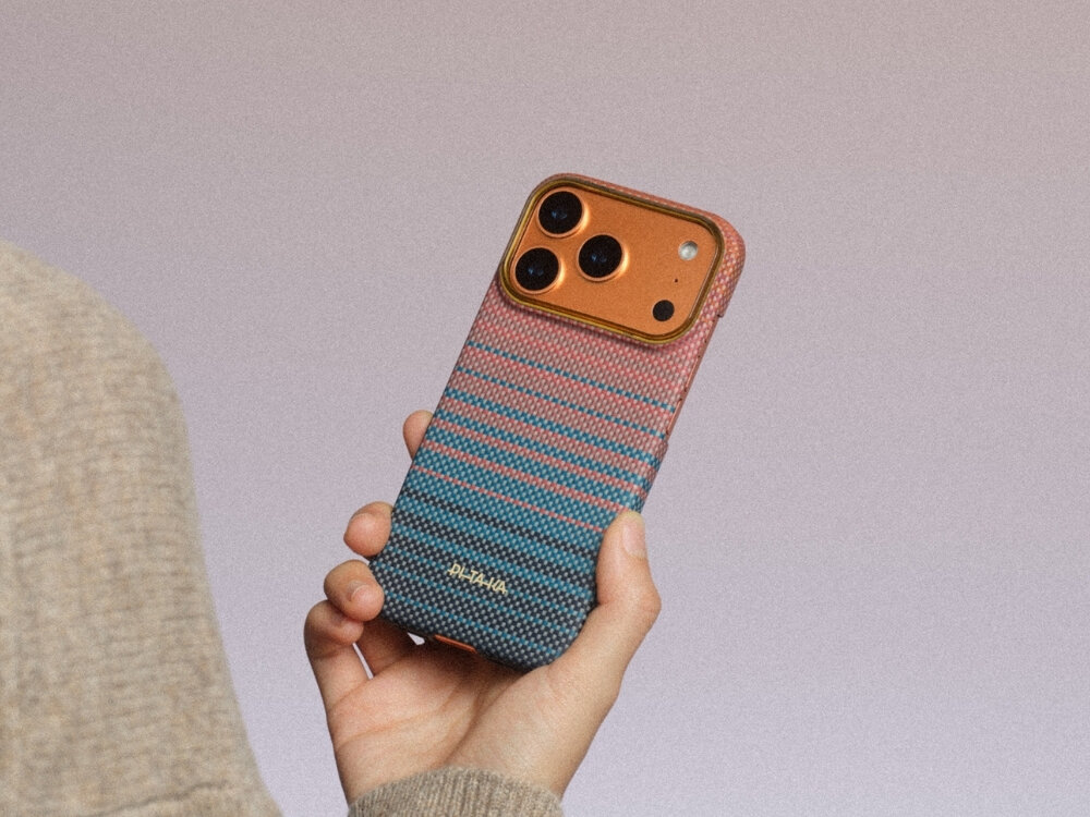 Osoba trzyma telefon w etui o kolorowym, gradientowym wzorze z widocznym napisem \'PITAKA\'. Telefon ma trzy kamery i błyszczący, pomarańczowy panel wokół aparatów.