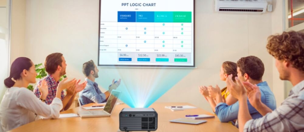 Grupa ludzi siedzi przy stole, patrząc na ekran z wyświetlonym wykresem zatytułowanym \'PPT LOGIC CHART\'. Na stole znajduje się projektor emitujący światło w kierunku ekranu.