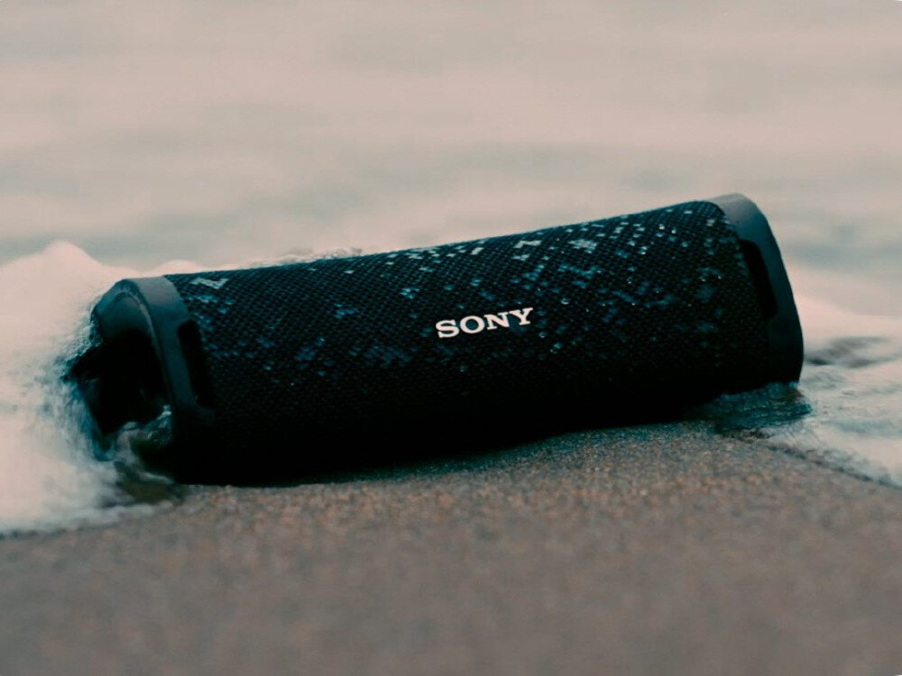 Czarny głośnik mobilny z logo \'SONY\' leży na mokrym piasku, częściowo zanurzony w wodzie.
