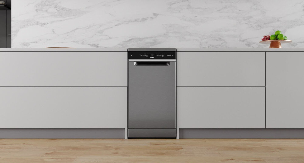 Zmywarka w kolorze inox wbudowana w nowoczesną kuchnię z białymi szafkami i marmurowym blatem. Na blacie stoi patera z owocami.