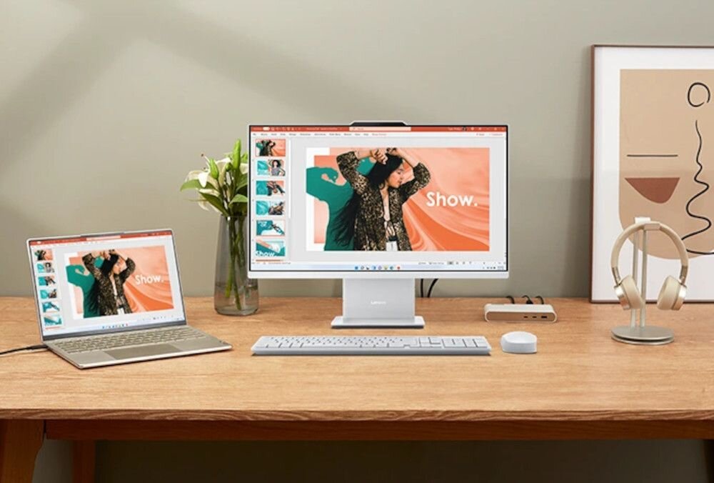 Na biurku znajduje się komputer All in One z dużym monitorem, klawiaturą i myszką, obok stoi laptop. Na ekranach obu urządzeń wyświetlana jest ta sama prezentacja z napisem \'Show.\'.