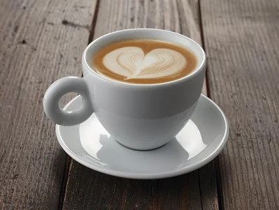 Biała filiżanka z kawą latte, na której powierzchni znajduje się wzór w kształcie serca, stoi na drewnianym stole.