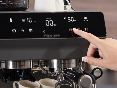 Panel sterowania ekspresu do kawy z wyświetlaczem pokazującym 10 sekund, 00 Bar i 50 ml. Logo Hisense widoczne na panelu, a ręka dotyka jednego z przycisków.
