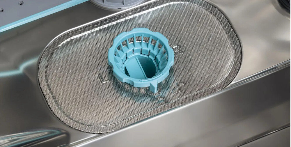 Wnętrze zmywarki z widocznym filtrem i niebieskim elementem plastikowym na metalowej siatce. W tle widać fragmenty metalowych elementów zmywarki.