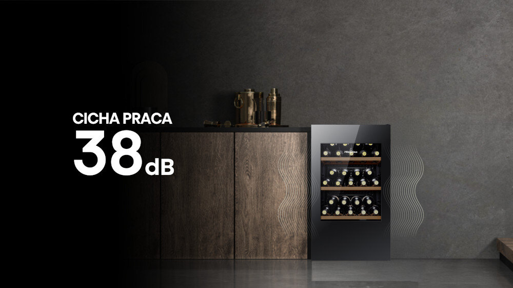 Na obrazie widoczna jest chłodziarka do wina z trzema półkami, wypełniona butelkami, obok drewnianej szafki. Po lewej stronie znajduje się tekst: \'CICHA PRACA 38 dB\'.
