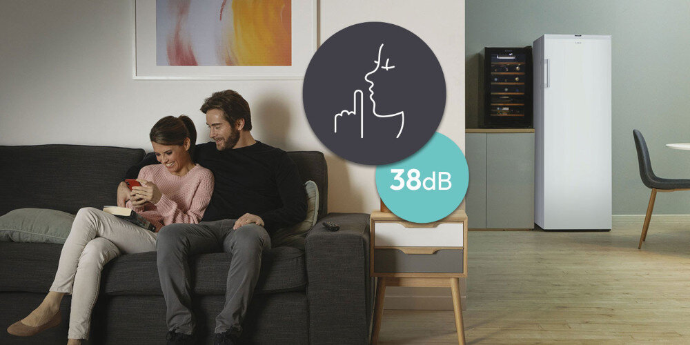 Para siedzi na kanapie w salonie, obok znajduje się zamrażarka szufladowa. Na obrazie widoczna jest ikona z symbolem ciszy i napis \'38dB\'.