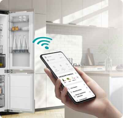 Osoba trzyma smartfon z aplikacją pokazującą funkcje lodówki, obok otwarta lodówka z widocznymi półkami i produktami. Nad smartfonem widoczna jest ikona sygnału Wi-Fi.