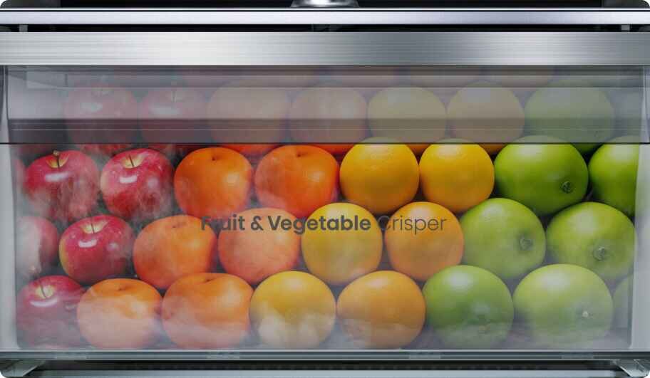 Wnętrze szuflady lodówki wypełnione jest owocami: czerwonymi jabłkami, pomarańczami i zielonymi jabłkami. Na szufladzie widoczny jest napis \'Fruit & Vegetable crisper\'.