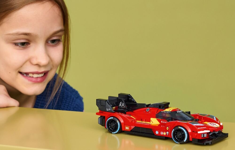 Na obrazie widać czerwony model samochodu wyścigowego z klocków LEGO z czarnymi i żółtymi detalami. W tle znajduje się osoba patrząca na model.