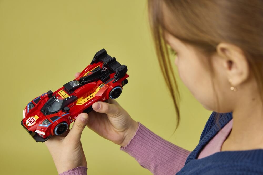 Osoba trzyma w rękach czerwony model samochodu wyścigowego z czarnymi i żółtymi elementami, wykonany z klocków LEGO. Na samochodzie widoczne są naklejki z numerem 51 i logo Ferrari.