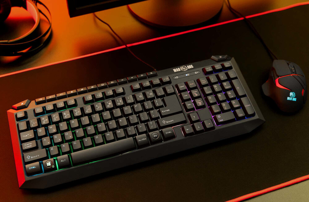 Na obrazie widoczna jest klawiatura z podświetleniem RGB oraz mysz komputerowa na ciemnym biurku. Na klawiaturze znajduje się logo \'MAD DOG\'.
