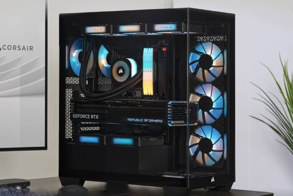 Obudowa komputera z przezroczystym panelem bocznym, wewnątrz widoczne podświetlane wentylatory i komponenty. Na obudowie widoczne są napisy: \'CORSAIR\', \'GEFORCE RTX\', \'REPUBLIC OF GAMERS\'.