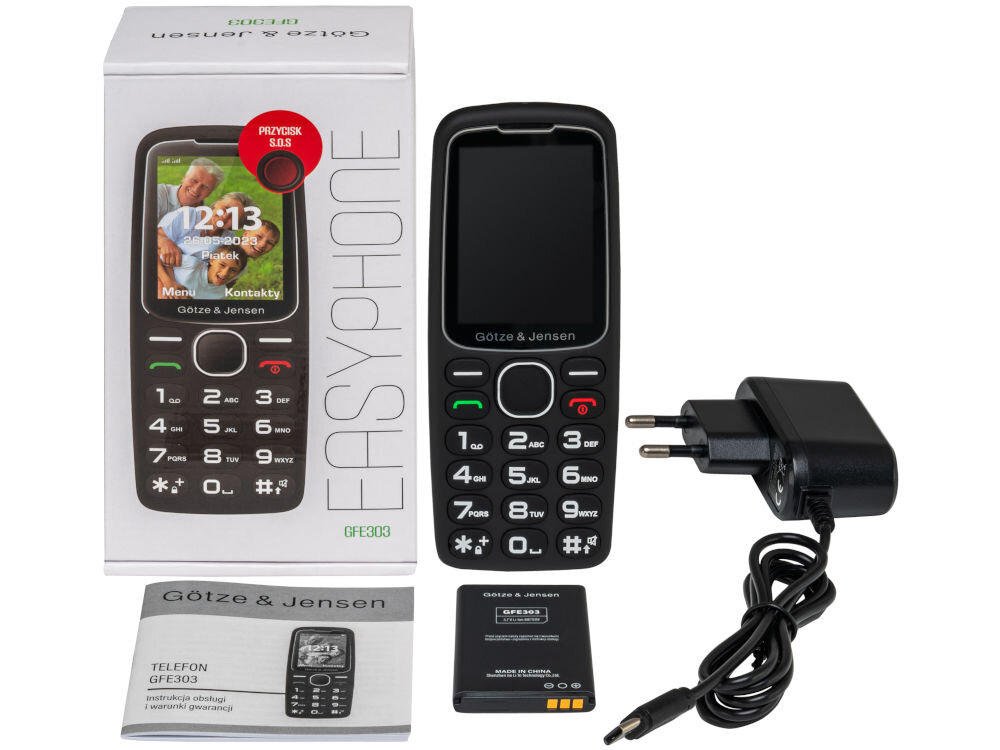 Na obrazie znajduje się czarny telefon Götze & Jensen GFE303 z dużymi przyciskami, obok którego leży ładowarka, bateria oraz instrukcja obsługi. W tle widoczne jest pudełko z napisem \'EASYPHONE\' i zdjęciem telefonu.