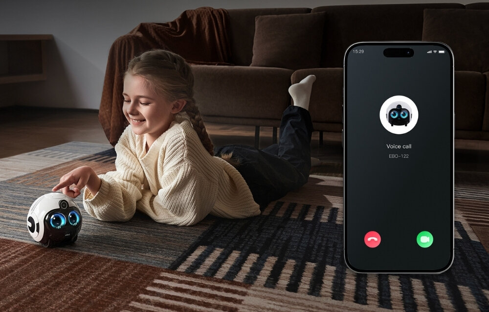 Dziecko leży na dywanie i dotyka białego robota z niebieskimi oczami. Obok znajduje się smartfon z ekranem pokazującym połączenie głosowe z ikoną robota i tekstem \'Voice call EBO-122\'.