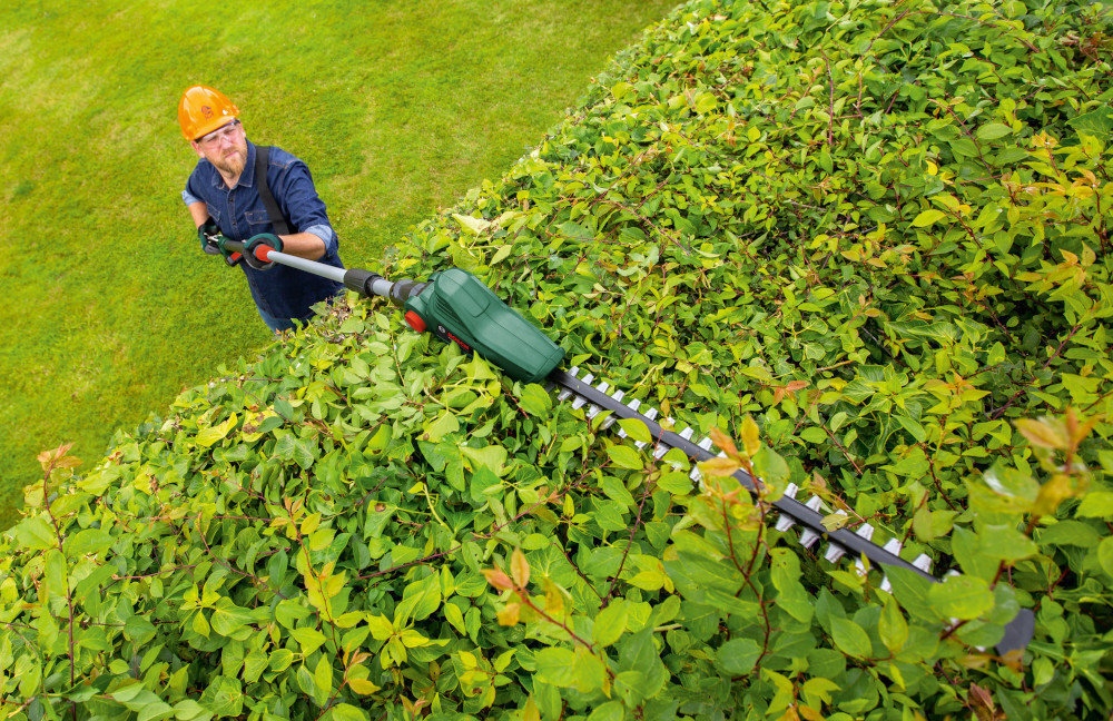 Nożyce do żywopłotu BOSCH UniversalHedgePole 18 akumulatorowe ogród trawnik żywopłot osoba przycina żywopłot waga 3,6 kg odpowiednie wyważenie komfort użytkowania wygodna bezpieczna praca pasek na ramię w zestawie odciąża ręce
