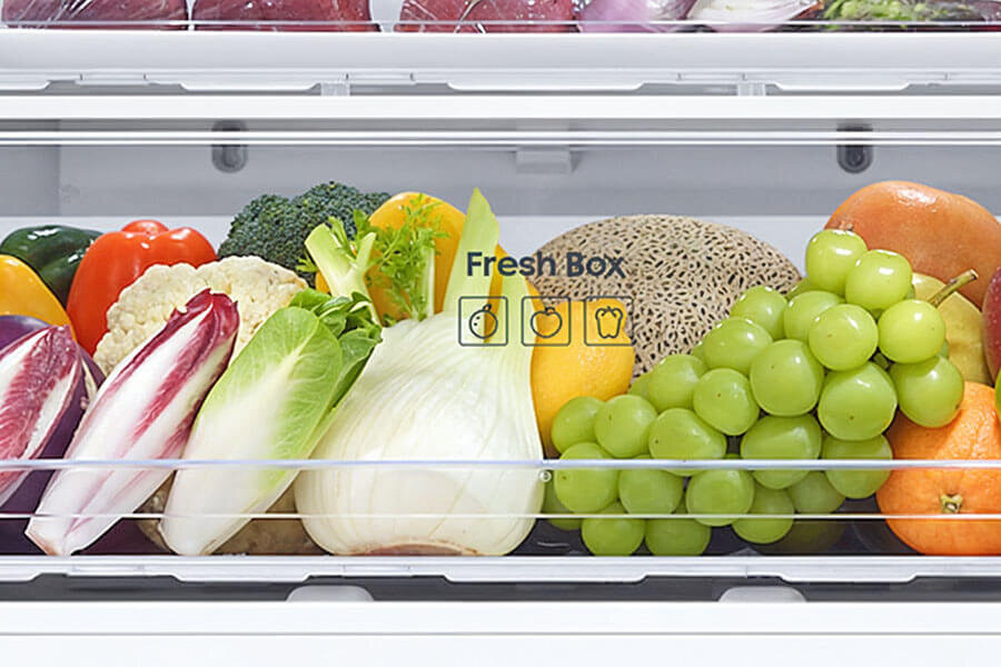 Zdjęcie - lodówka RB53DG706AB1 - Media Expert - Fresh Box W lodówce znajduje się szuflada z różnorodnymi warzywami i owocami, takimi jak winogrona, pomarańcze, brokuły i melon. Na szufladzie widoczny jest napis \'Fresh Box\' z ikonami owoców i warzyw.