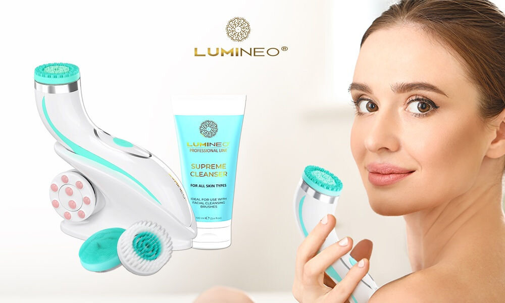 Na obrazie widoczna jest szczoteczka soniczna do twarzy w kolorze turkusowym oraz żel do twarzy z napisem \'LUMINEO PROFESSIONAL LINE SUPREME CLEANSER FOR ALL SKIN TYPES\'. W tle znajduje się kobieta trzymająca szczoteczkę przy twarzy.