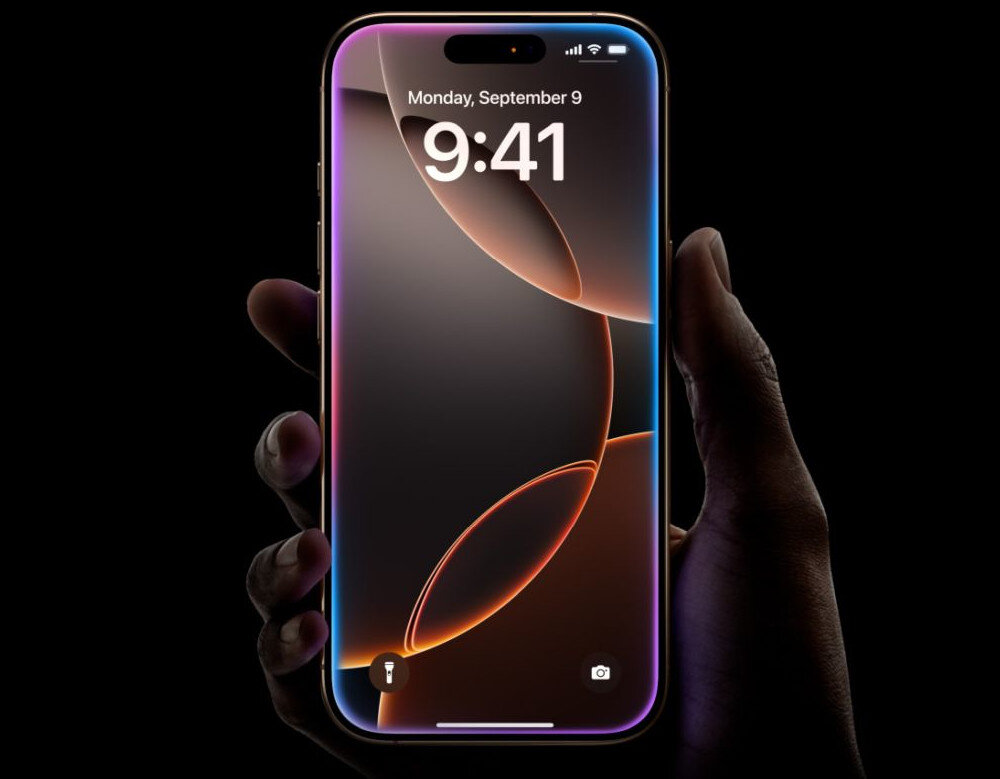 Osoba trzyma smartfon z wyświetlaczem pokazującym godzinę 9:41 i datę Monday, September 9. Ekran ma abstrakcyjną grafikę z kolorowymi liniami i ikonami aparatu oraz latarki na dole.