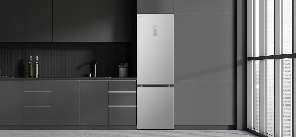Nowoczesna kuchnia z ciemnymi szafkami i srebrną lodówką. Lodówka ma prosty, elegancki design i jest umieszczona obok zlewu z kranem.