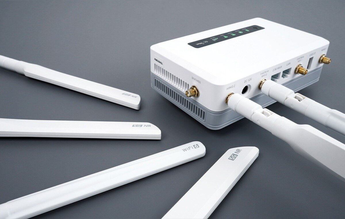Biały router od tyłu z odłączonymi płaskimi antenami z napisami 5G NR i WiFi 6 leżącymi na szarym tle