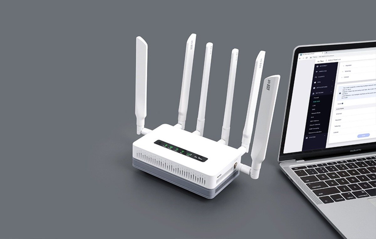 Biały router z sześcioma pionowymi antenami stoi na szarym tle obok otwartego laptopa z panelem admina