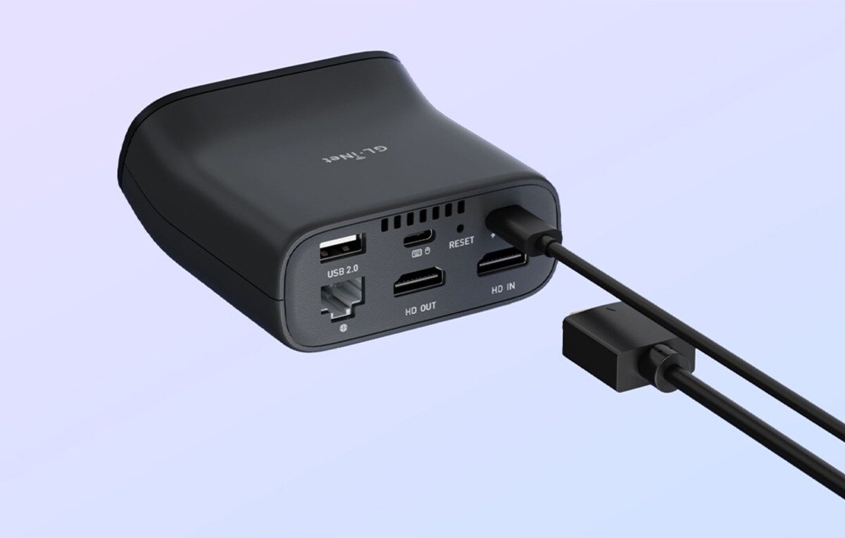 Czarny przełącznik KVM z widocznymi portami: USB 2.0, HDMI, oraz przyciskiem reset. Na obudowie znajduje się napis \'GL.iNet\'.