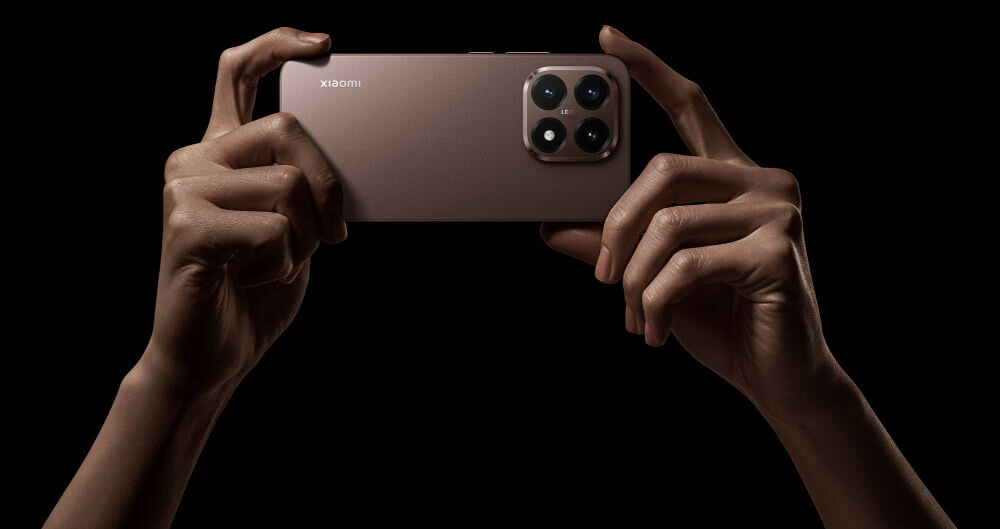 Osoba trzyma smartfon z trzema widocznymi obiektywami aparatu i logo \'xiaomi\' na obudowie. Tło jest czarne, co podkreśla sylwetkę urządzenia.