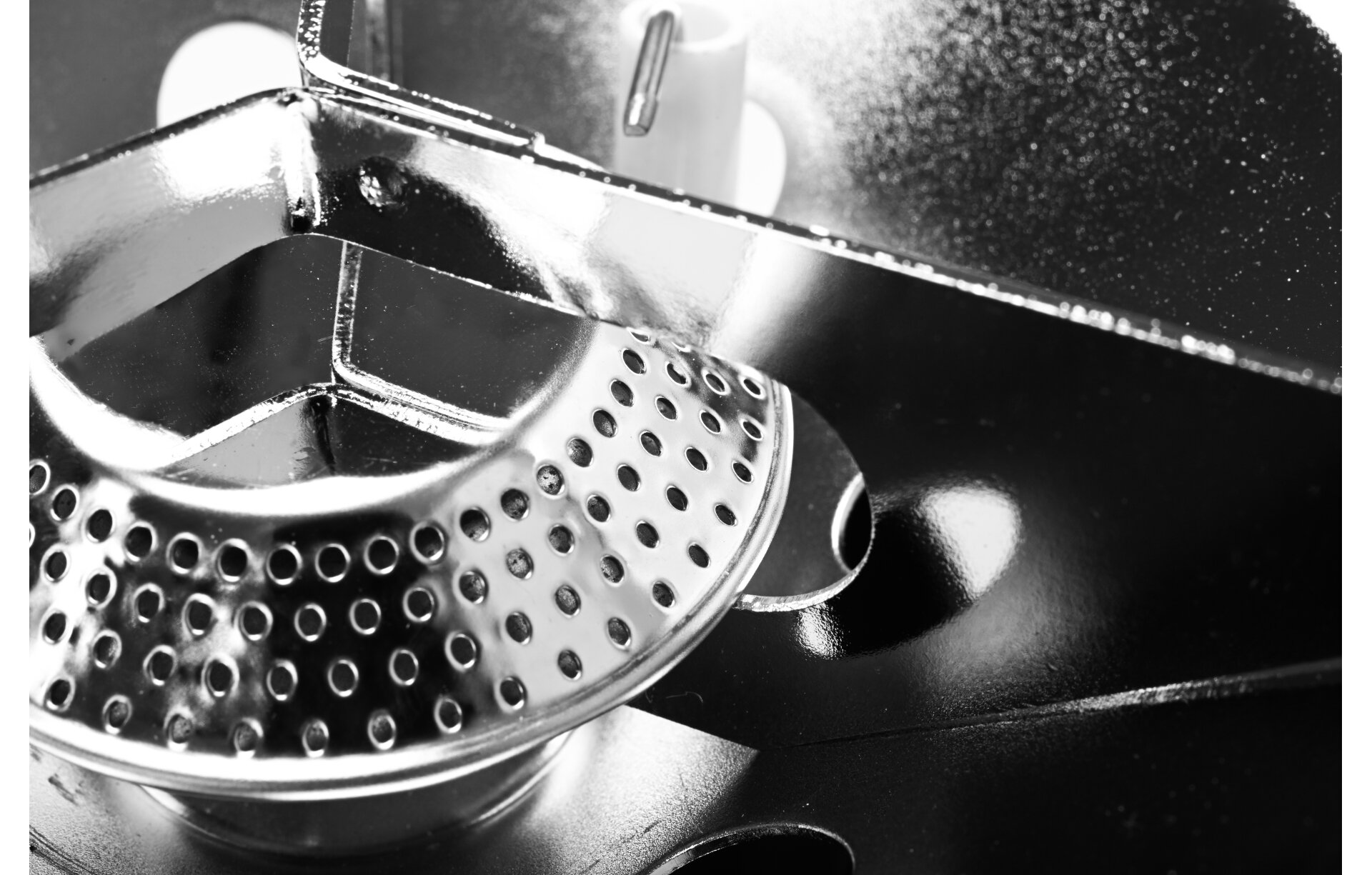 Zbliżenie na metalowy element kuchenki turystycznej z otworami wentylacyjnymi i błyszczącą powierzchnią.