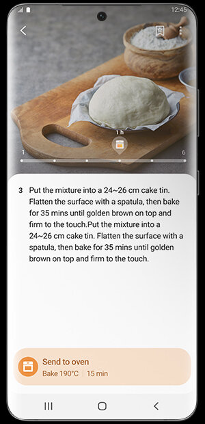 Piecz ciasto razem z aplikacją SmartThings Na ekranie smartfona widoczny jest przepis kulinarny z instrukcją: \'Put the mixture into a 24~26 cm cake tin. Flatten the surface with a spatula, then bake for 35 mins until golden brown on top and firm to the touch.\' Na dole ekranu znajduje się przycisk z napisem \'Send to oven Bake 190°C | 15 min\'.