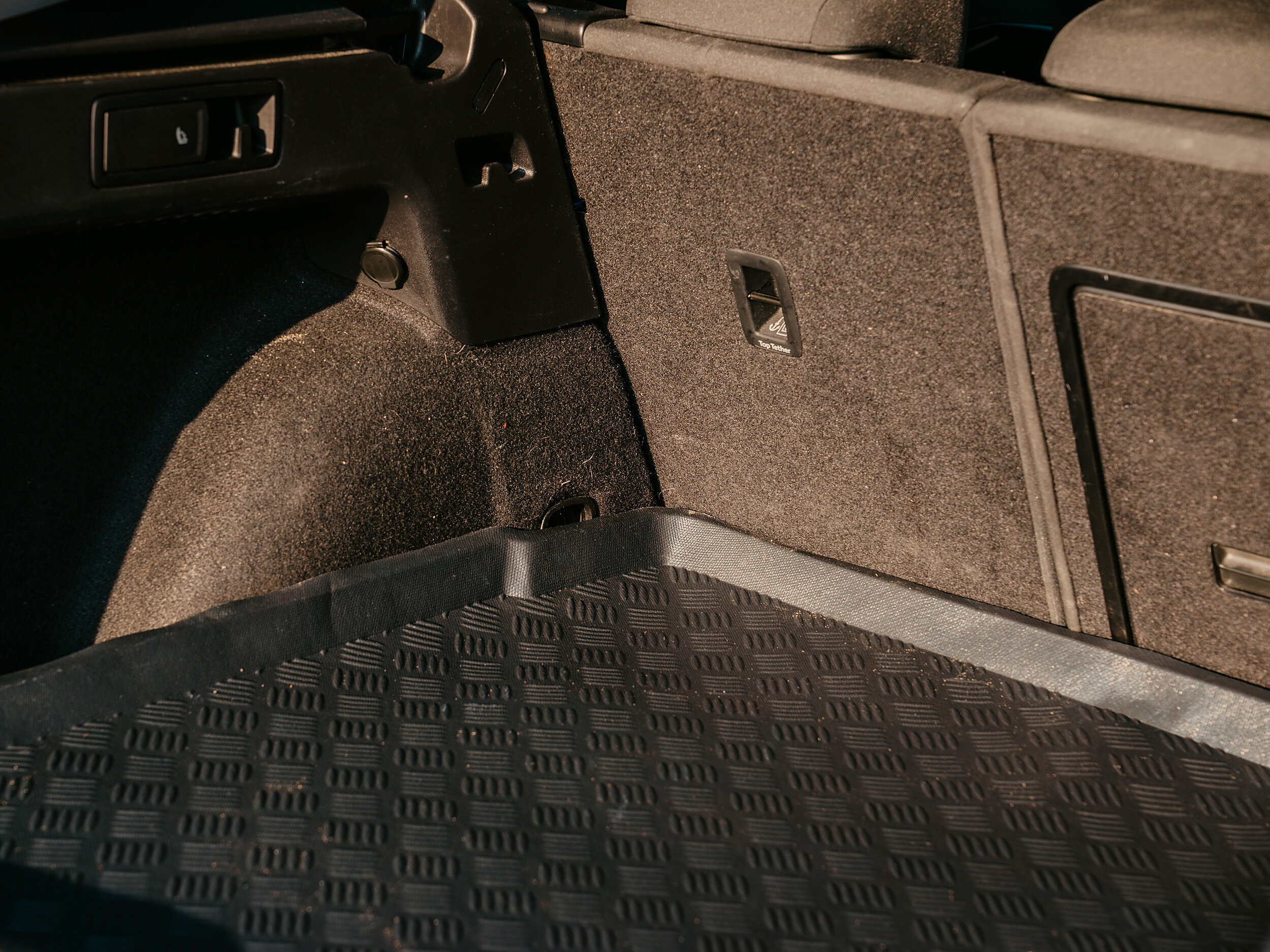 Wnętrze bagażnika samochodowego z matą ochronną o podwyższonych krawędziach i wzorem kratki. Ściany bagażnika są wyłożone materiałem tekstylnym, a na jednej z nich znajduje się uchwyt.