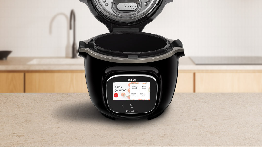 Czarny multicooker z otwartą pokrywą stoi na blacie kuchennym. Na wyświetlaczu widoczny jest tekst: \'Co dziś ugotujemy?\' oraz logo \'Tefal\'.