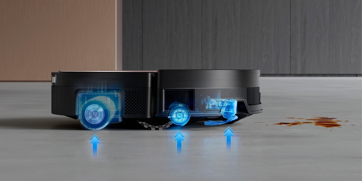 Czarny robot sprzątający na podłodze z wizualizacją działania kół i mechanizmów wewnętrznych. Obok robota widoczna jest plama na podłodze.