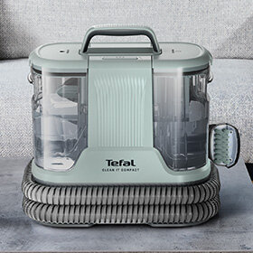 Odkurzacz piorący w kolorze miętowym z przezroczystymi zbiornikami po bokach i uchwytem na górze. Na przedniej części widoczne jest logo \'Tefal Clean It Compact\'.