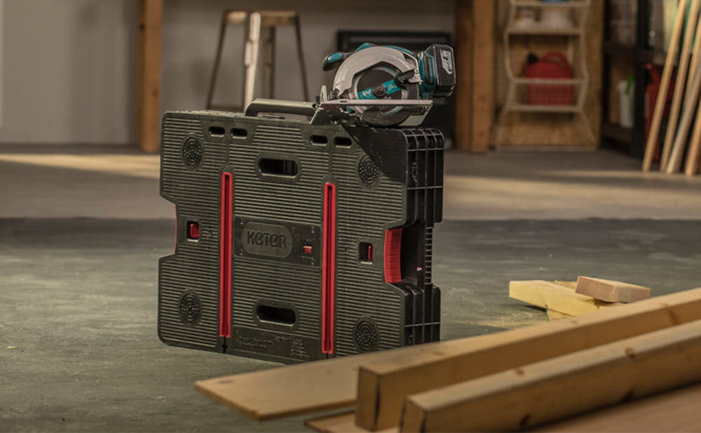 Stół warsztatowy składany KETER Folding Work Table 453 kg złożony stół stoi na podłodze w warsztacie składany stół warsztatowy prace montażowe, remontowe i stolarskie stabilna powierzchnia robocza ułatwia realizację codziennych zadań pozwala zachować ciągłość pracy