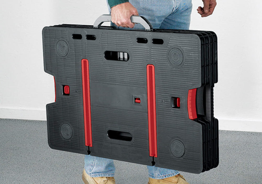 Stół warsztatowy składany KETER Folding Work Table 453 kg jasne tło osoba niesie w dłoni złożony stół trzyma za uchwyt system składania przygotowanie stołu do pracy w zaledwie kilka sekund stół można równie szybko złożyć wbudowany uchwyt waga 12,25 kg stabilność mobilność