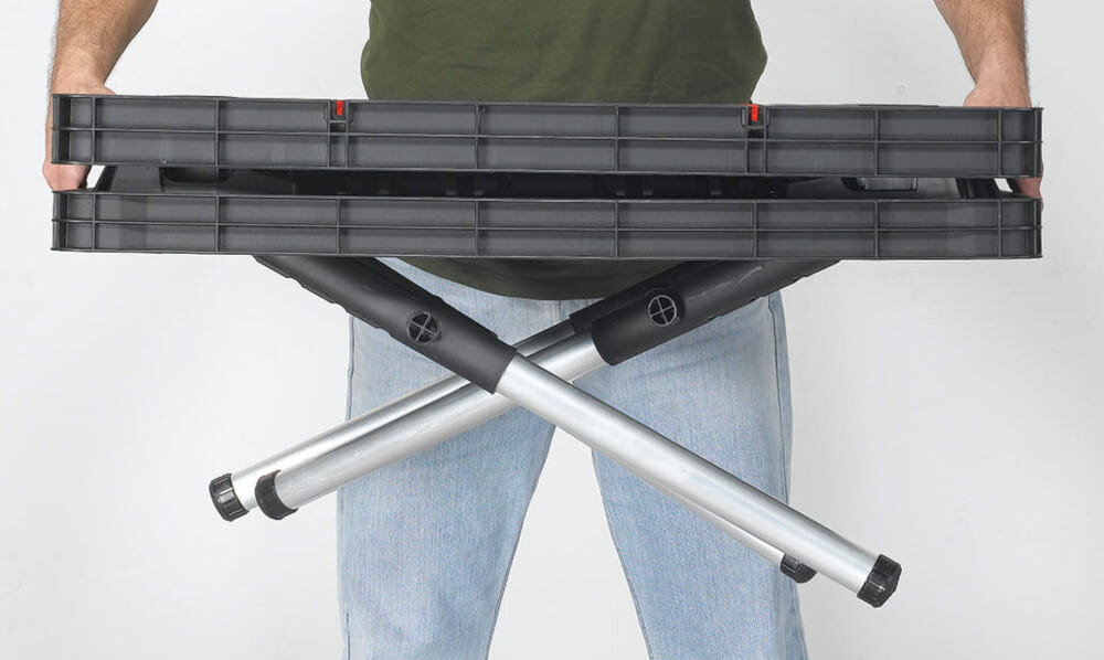 Stół warsztatowy składany KETER Folding Work Table 453 kg jasne tło osoba trzyma w pół złożony stół w dłoniach uniwersalna konstrukcja wysokość robocza około 75,5 cm wygodna pozycja podczas pracy zmniejsza obciążenie pleców lepsza wydajność większa kontrola