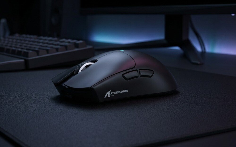 Mysz ATTACK SHARK X11 Mysz komputerowa widziana z boku, stojąca na podkładce obok klawiatury i monitora, z widocznym profilowanym kształtem oraz bocznymi przyciskami