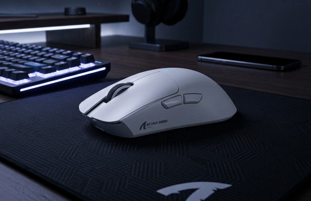 Mysz ATTACK SHARK X11 Mysz komputerowa widziana z boku, stojąca na podkładce obok klawiatury i monitora, z widocznym profilowanym kształtem oraz bocznymi przyciskami