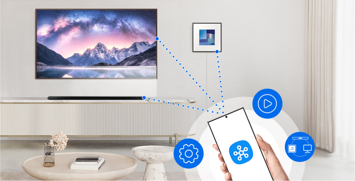 W salonie znajduje się telewizor z krajobrazem górskim na ekranie, a przed nim soundbar. W prawym dolnym rogu widoczny jest smartfon z ikonami ustawień, odtwarzania i połączenia, sugerującymi integrację z urządzeniami.