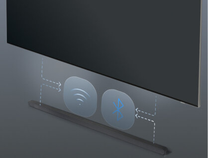 Obraz przedstawia soundbar umieszczony pod telewizorem, z ikonami Wi-Fi i Bluetooth wskazującymi na bezprzewodowe połączenie. Soundbar jest w kolorze ciemnym, a tło jest szare.