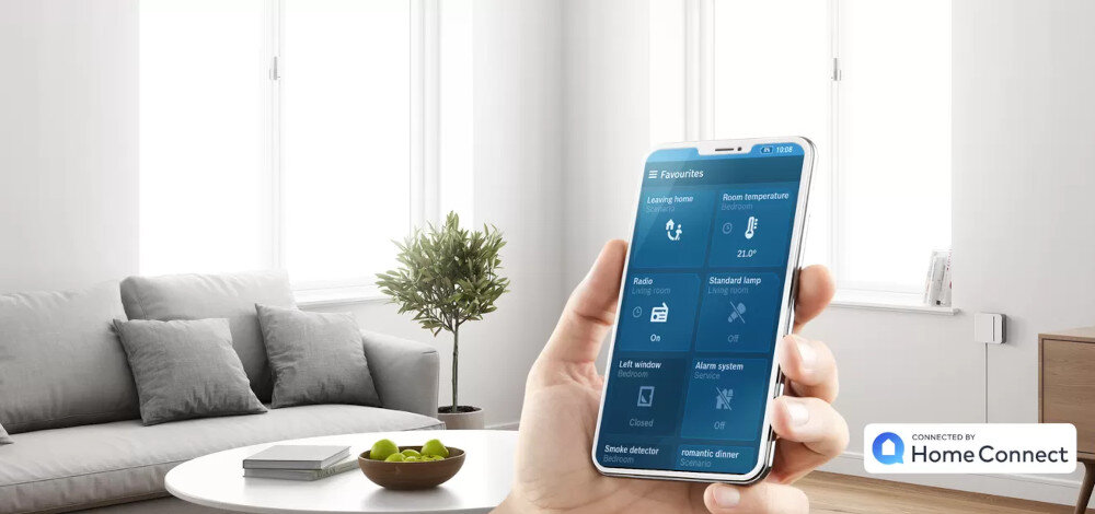Osoba trzyma smartfon z aplikacją HomeConnect, na ekranie widoczne są opcje sterowania domem. W tle znajduje się jasny salon z sofą, stolikiem i rośliną.