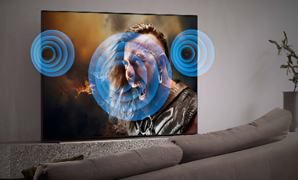 Telewizor wyświetla dynamiczną scenę z postacią, wokół której widoczne są niebieskie fale dźwiękowe. W tle znajduje się nowoczesne wnętrze z sofą i rośliną.