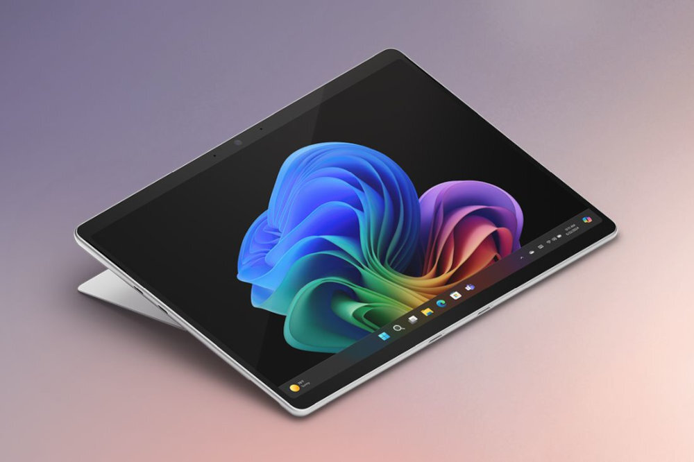 Na obrazie widoczny jest laptop z ekranem dotykowym, na którym wyświetlany jest kolorowy motyw systemu Windows. Urządzenie jest ustawione w pozycji stojącej na powierzchni o gradientowym tle.