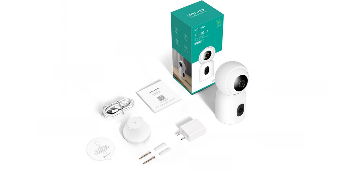 Na obrazie znajduje się biała, obrotowa kamera wewnętrzna oraz jej akcesoria, takie jak kabel, zasilacz, uchwyt montażowy i instrukcja. Obok kamery widoczne jest pudełko z napisem \'imilab SC330-D\'.