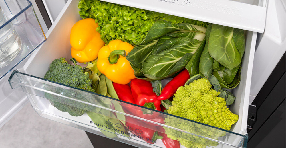 Szuflada lodówki wypełniona różnymi warzywami, takimi jak papryka, sałata, brokuł i romanesco. Na szufladzie widoczny jest napis \'Fruit & Vegetable Box\'.